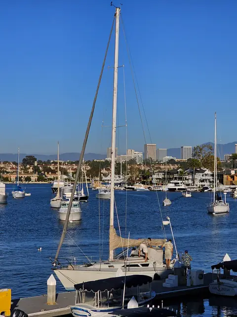 Sailboats moored in Newport Harbor with Newport Beach homes and hills behind